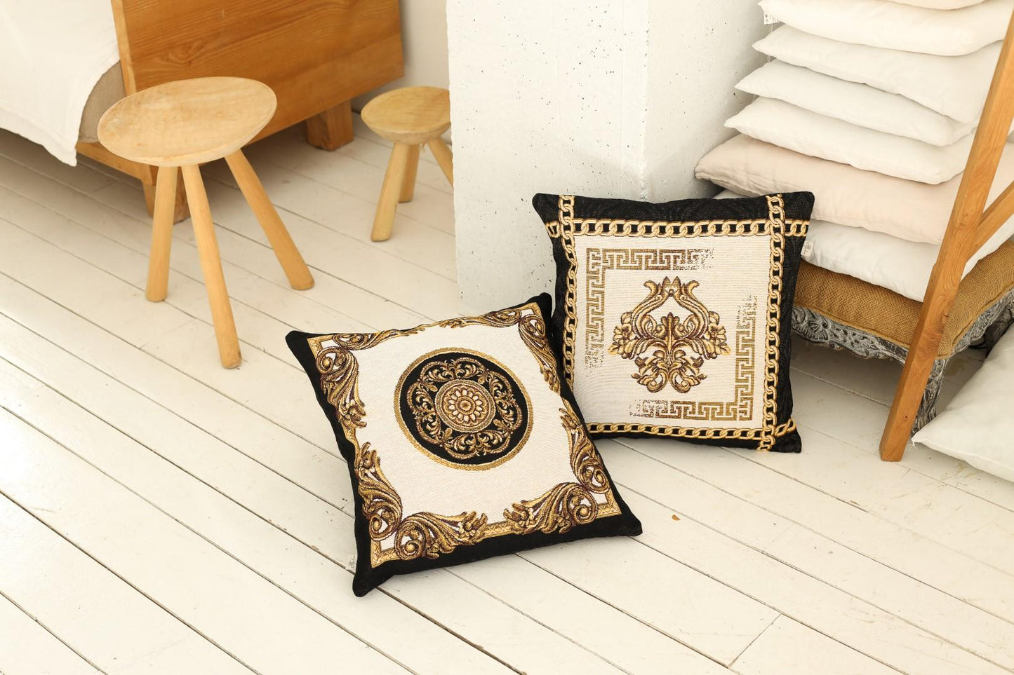 Two baroque tapestry pillows with gold patterns placed on a wooden floor in a cozy bedroom setting.