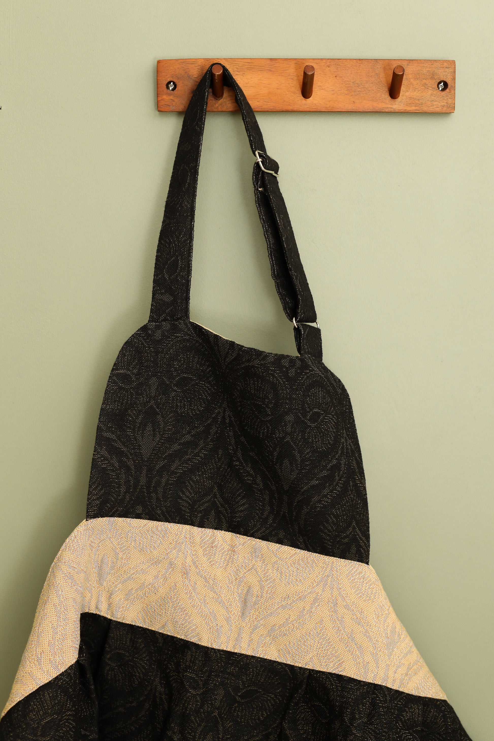 Black and beige baroque apron hanging on a wooden wall hook, adjustable neck strap visible
