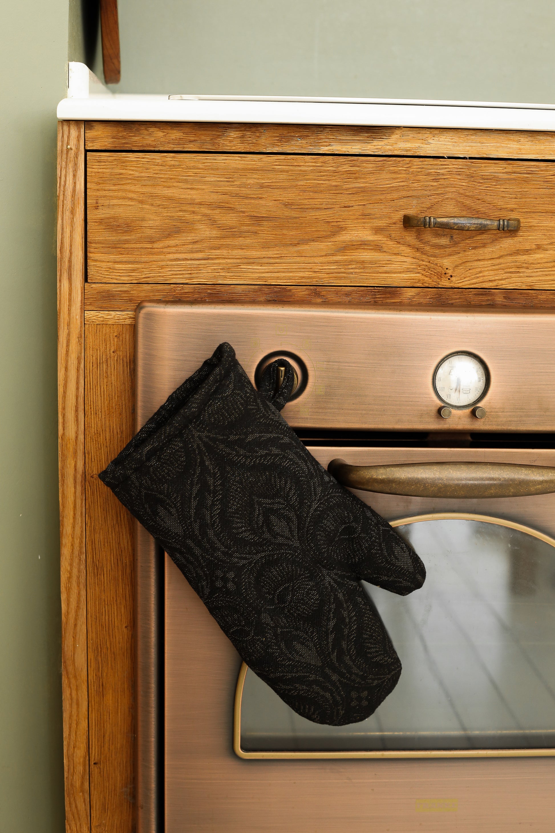 Black baroque oven mitt hanging on a vintage oven handle