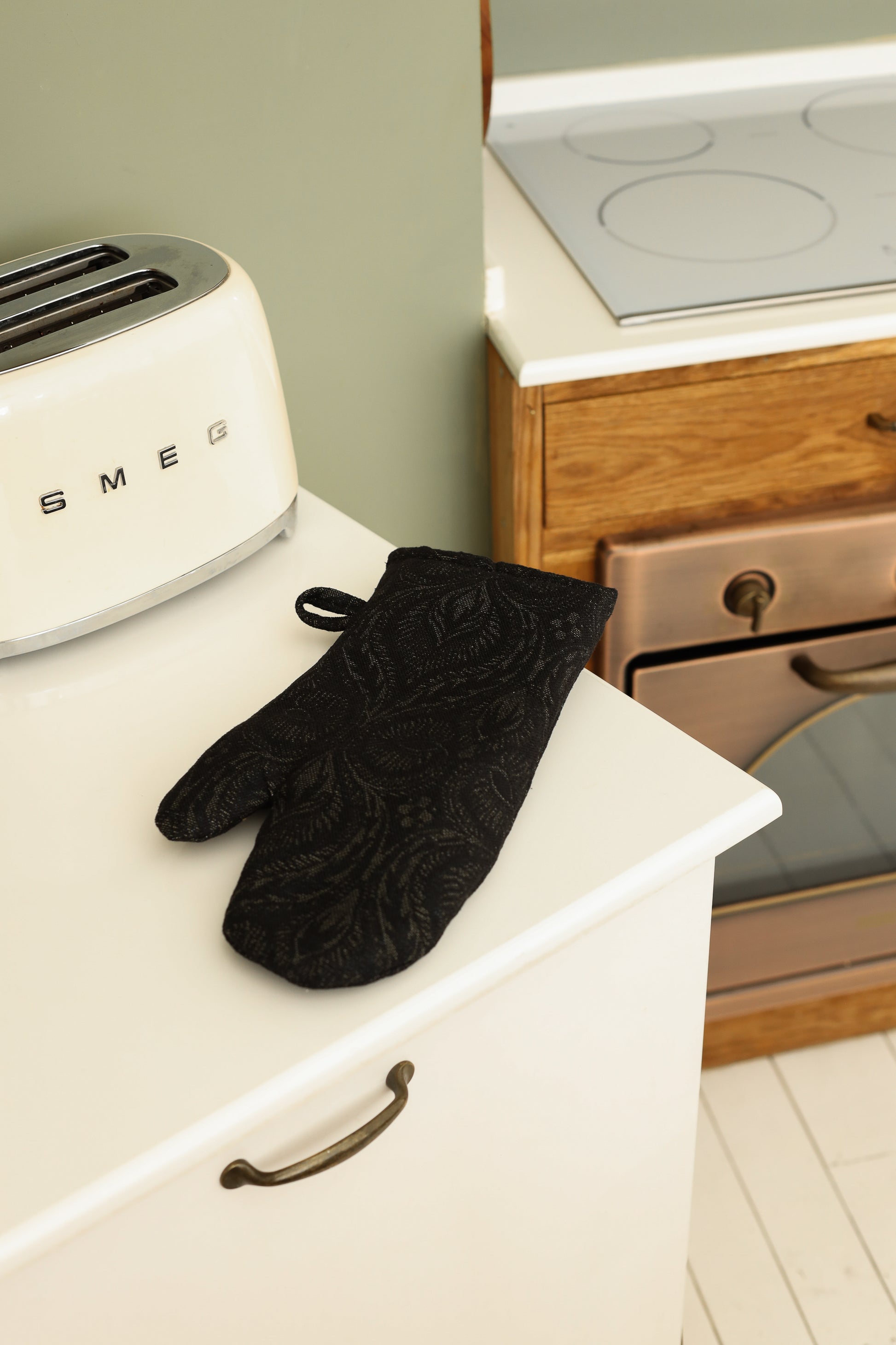 Black baroque oven mitt placed on a white kitchen countertop near an oven