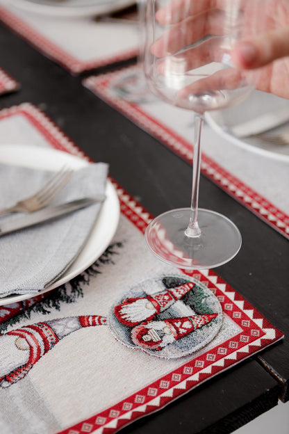 Christmas tapestry placemat with gnomes and snowy cottage placed under plate, napkin, and wine glass