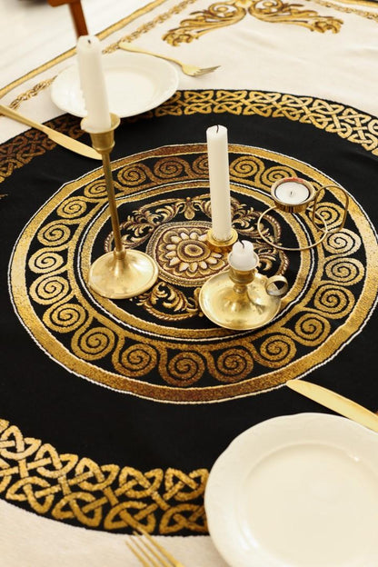 Close-up of baroque tapestry tablecloth with ornate gold medallion pattern, decorated with brass candle holders and table setting.