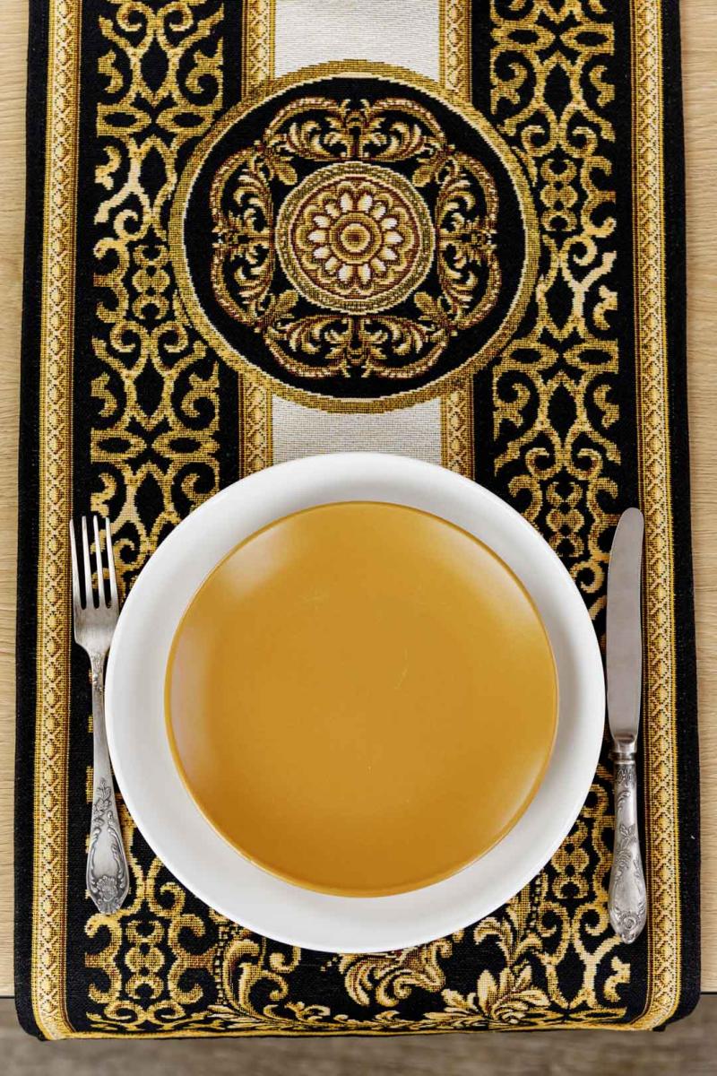Elegant table setting with a black and gold baroque tapestry placemat, white plate, fork, and knife.