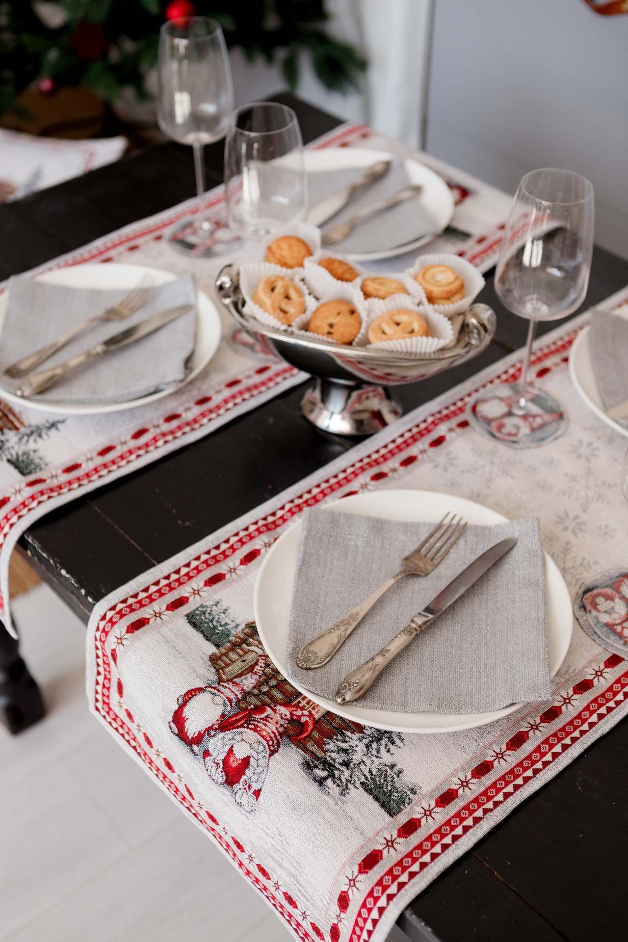 Festive dining table featuring woven Christmas gnome runners and pastries in a silver serving bowl.