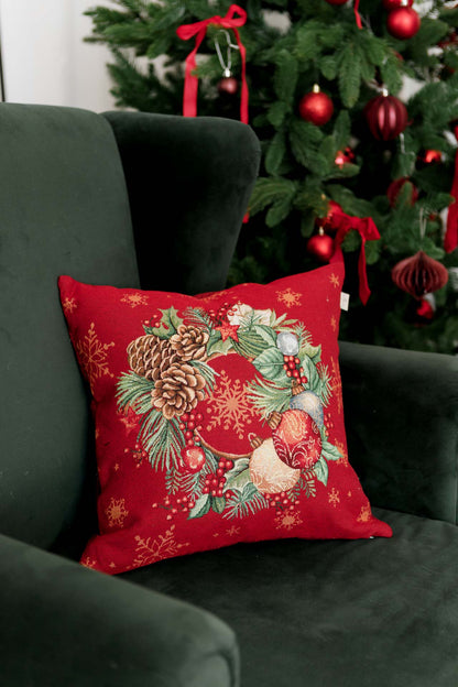 Festive wreath pillow cover on a green armchair near a decorated Christmas tree.