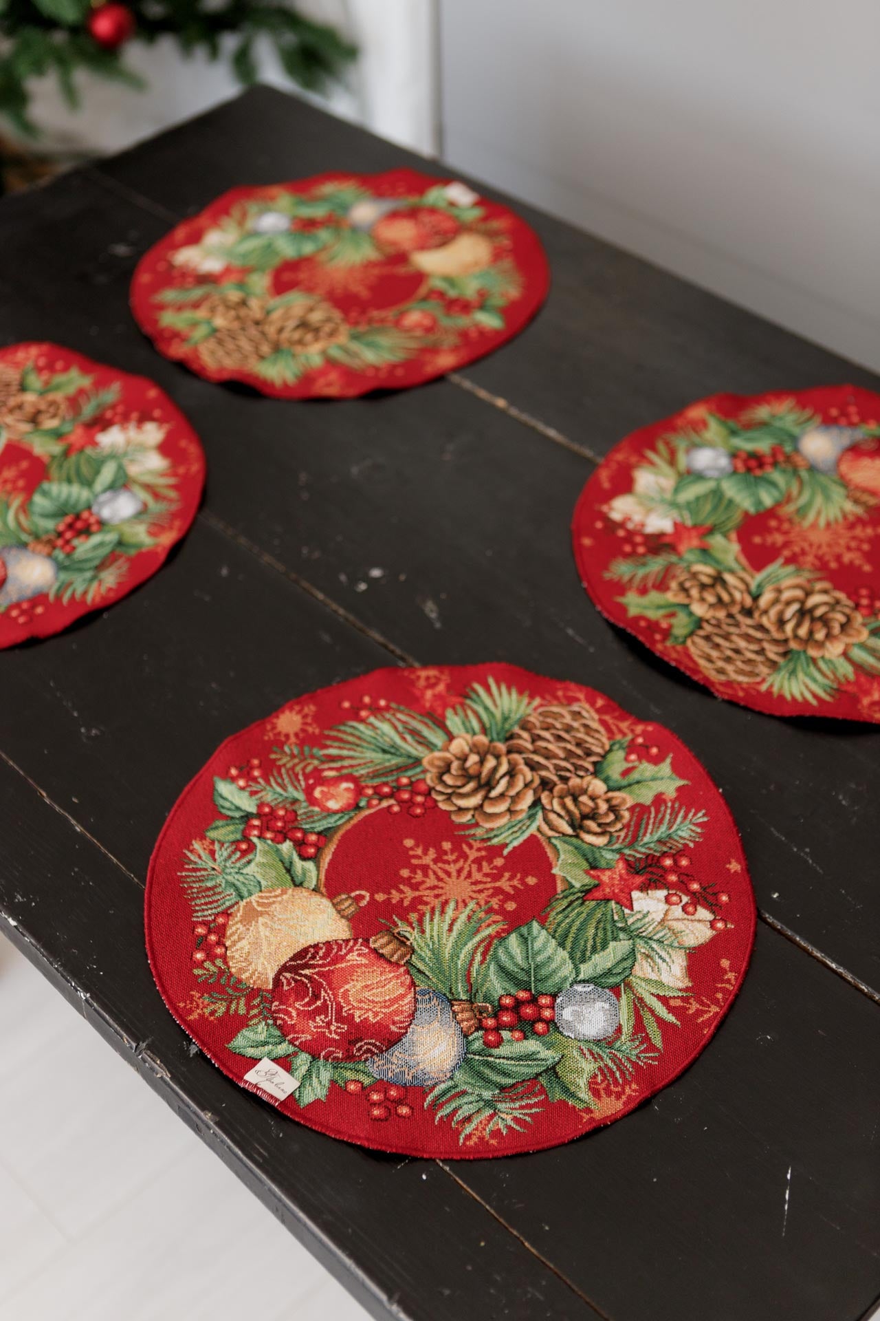 Holiday dining setup with round red tapestry placemat and pinecone motif