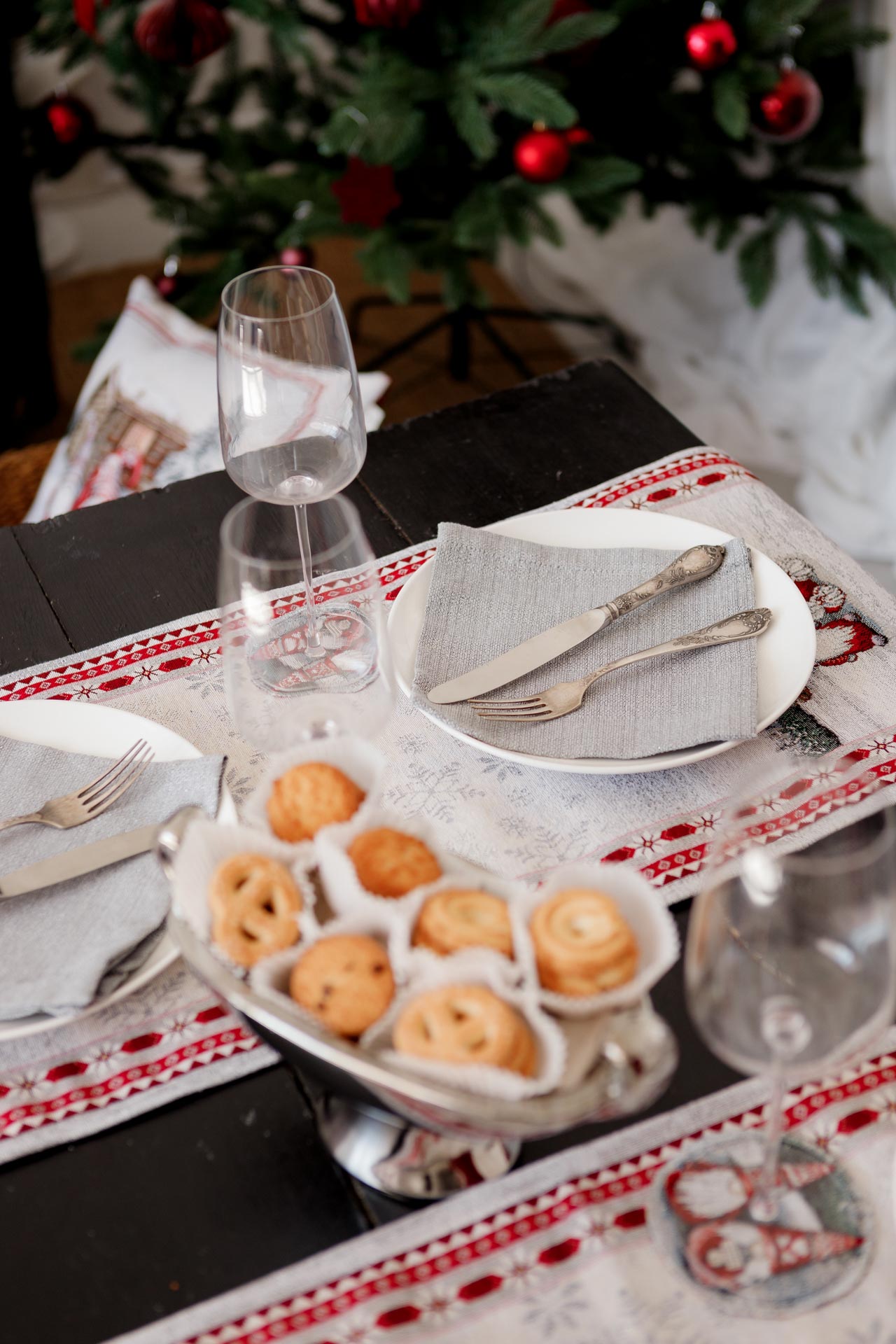 Holiday place setting on Christmas tapestry table runner with winter gnome scene and red border.