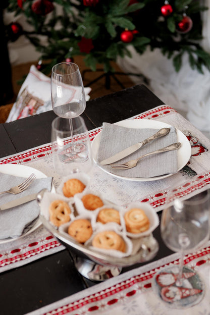 Holiday place setting on Christmas tapestry table runner with winter gnome scene and red border.