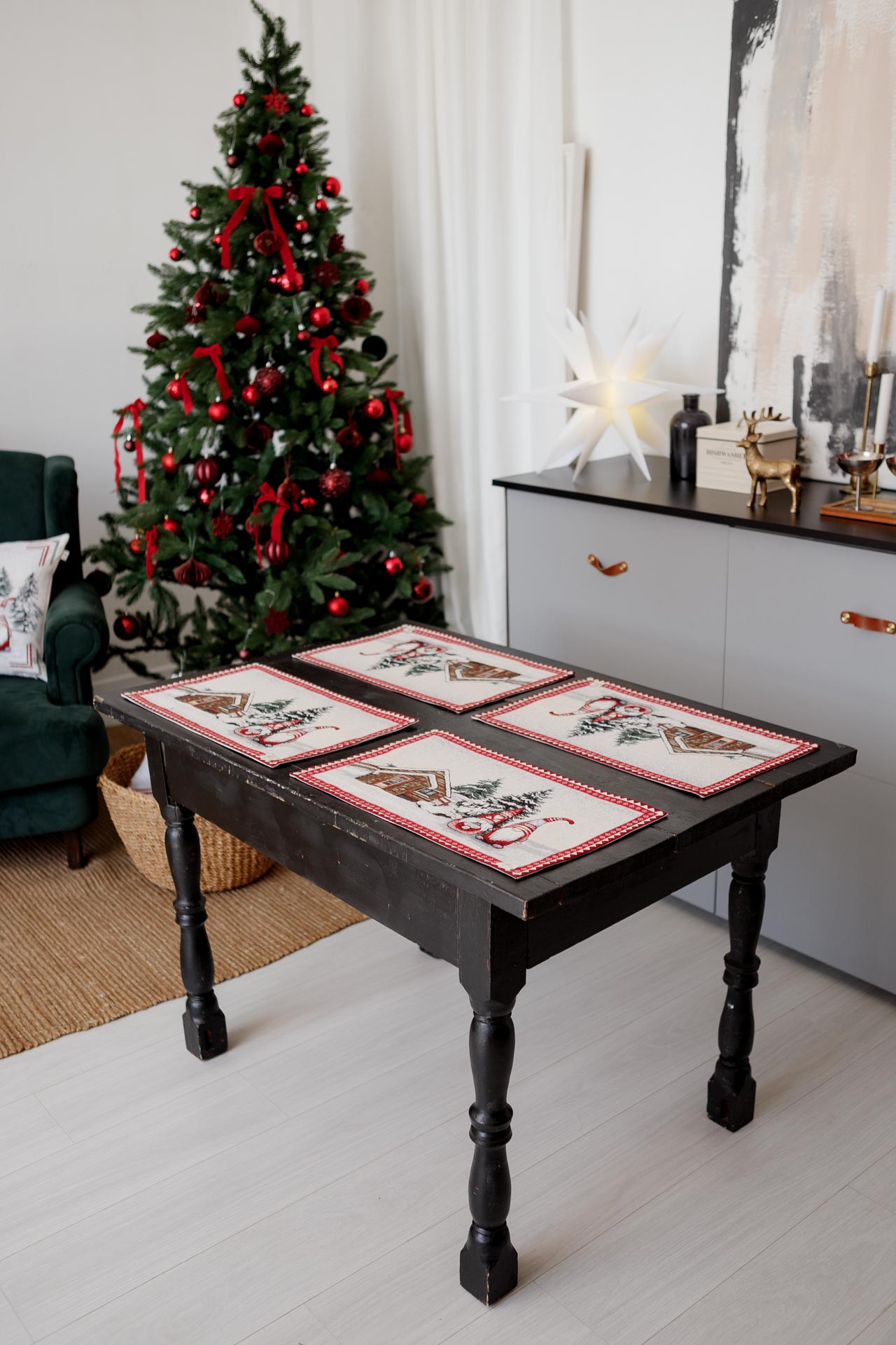 Set of four Christmas gnome tapestry placemats displayed on a rustic dark wooden table near a decorated Christmas tree