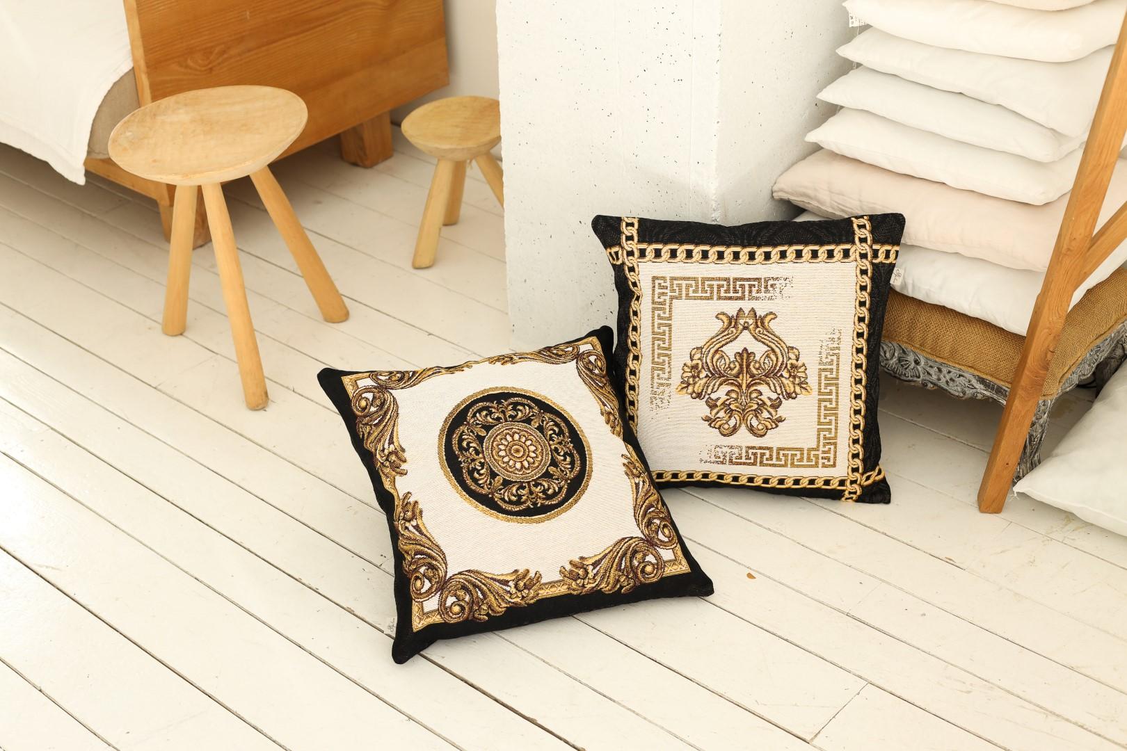 Two baroque tapestry pillows with gold patterns placed on a wooden floor in a cozy bedroom setting.