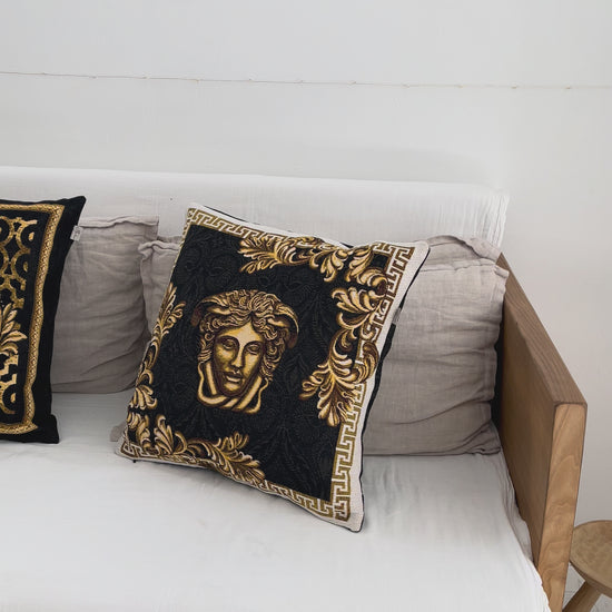 Black and gold baroque tapestry pillowcase with Medusa design styled on a white sofa in a luxury interior