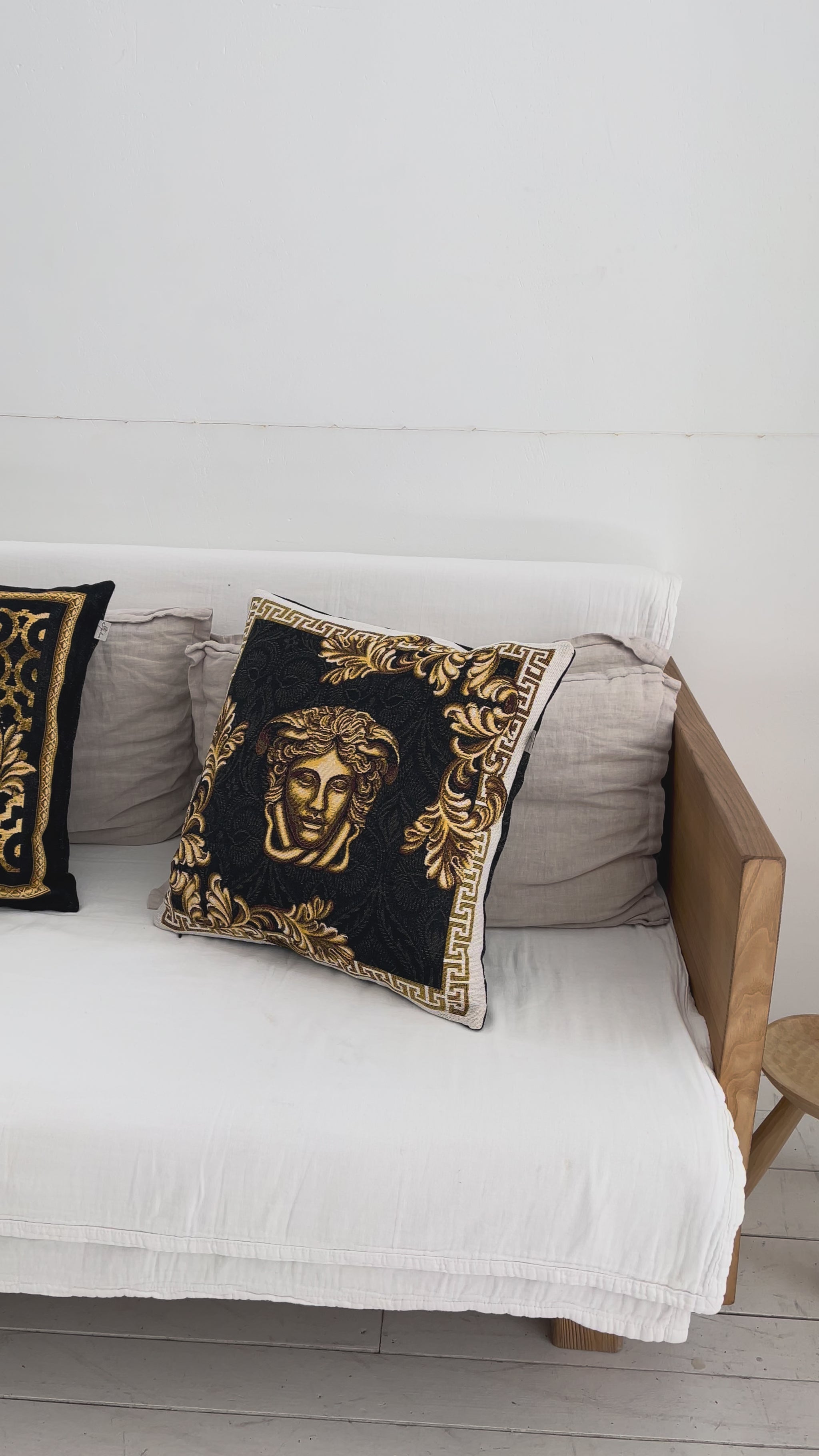 Black and gold baroque tapestry pillowcase with Medusa design styled on a white sofa in a luxury interior