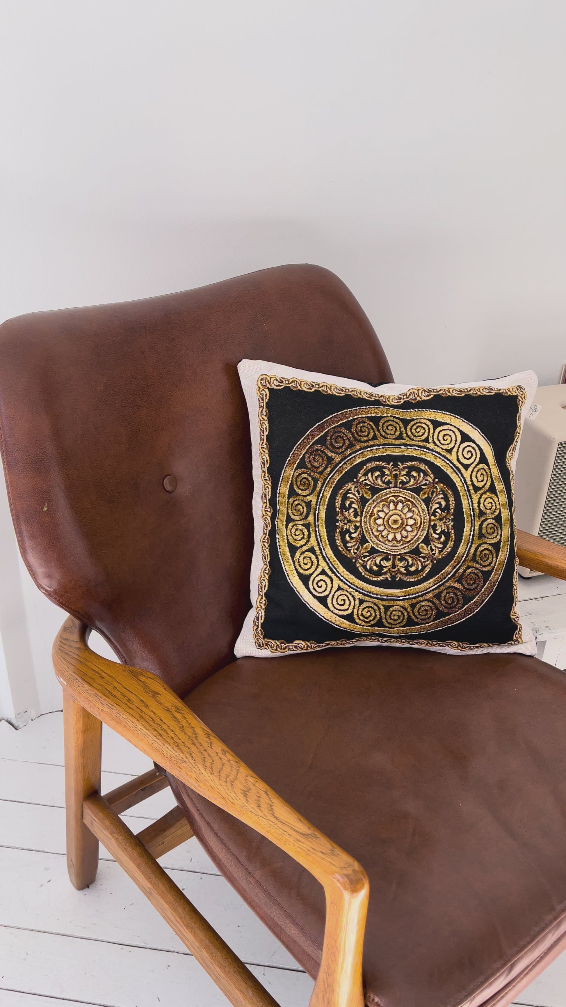 Video of black and gold baroque tapestry pillow placed on a brown leather chair in a modern interior.